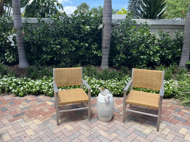 Paver patio with cane chairs framed by palms and white flowering border