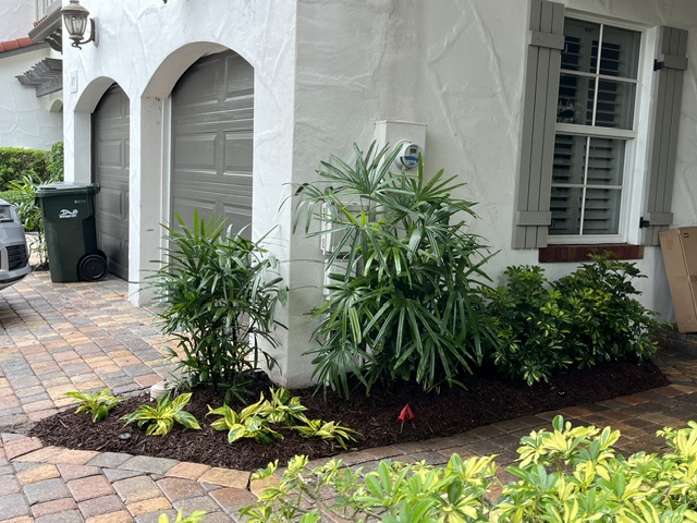 Stucco home with arched garages framed by hand-shaped tropical shrubs and palms in Palm Beach County